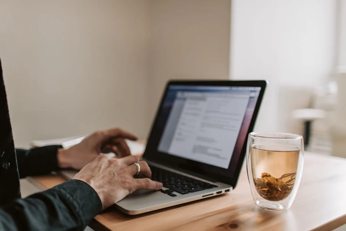 Adult working on laptop with a cup of tea, showcasing remote work lifestyle.